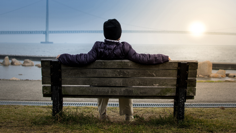 Picture of a man sitting on a bench on the beach watching the sunset