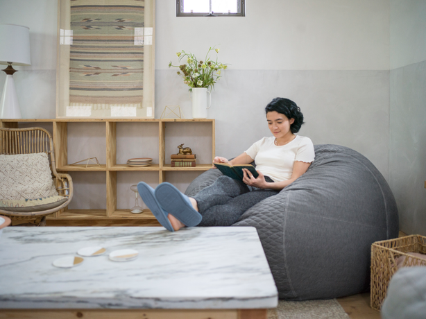 Woman sitting on a grey bean bag with her feet up on a coffee table reading a book