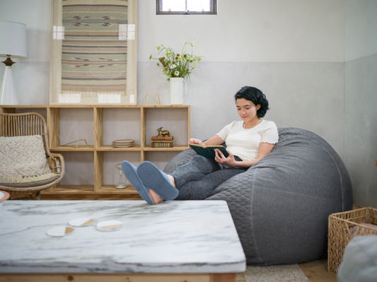 Woman sitting on a grey bean bag with her feet up on a coffee table reading a book