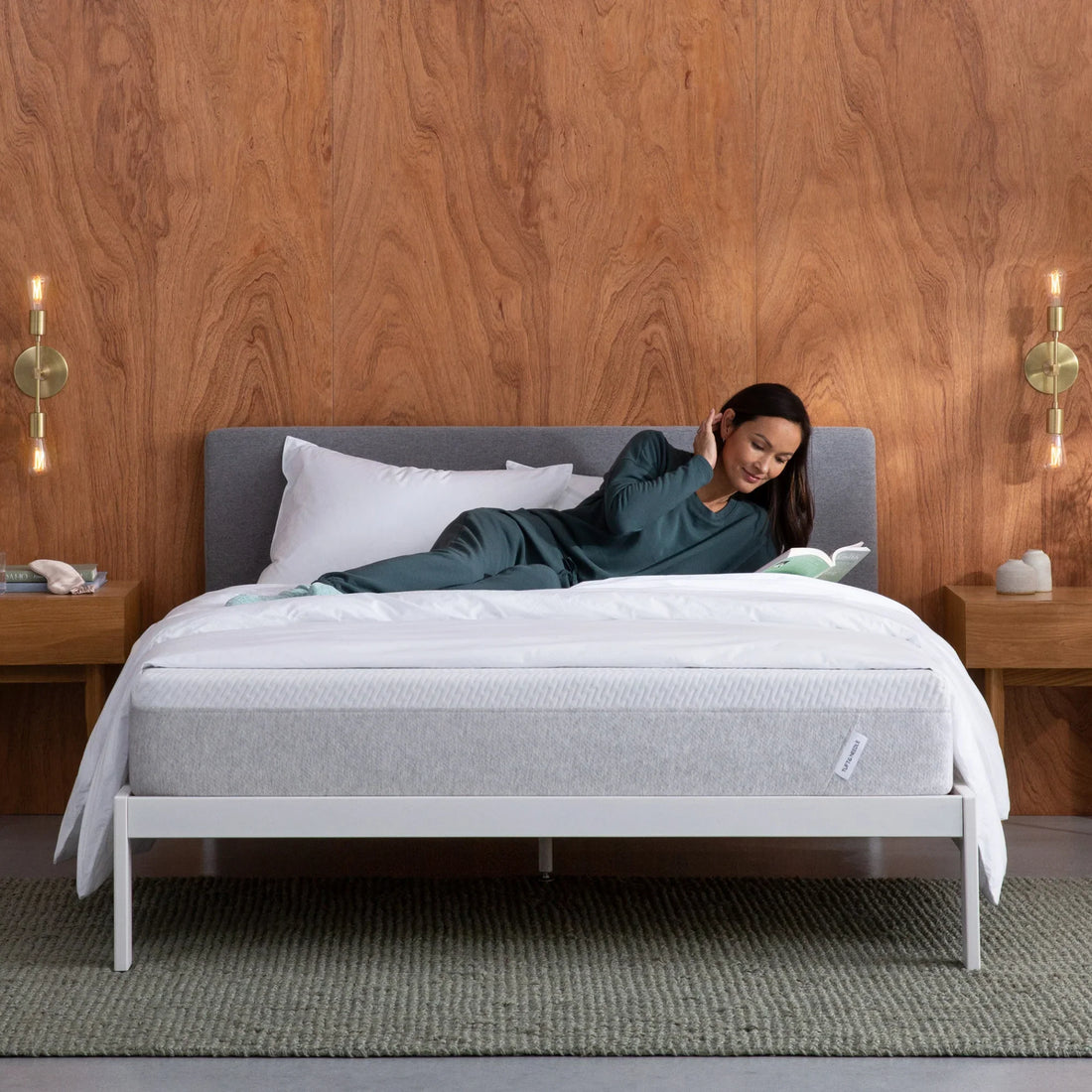 Woman laying sideways on a Tuft & Needle mattress reading a book