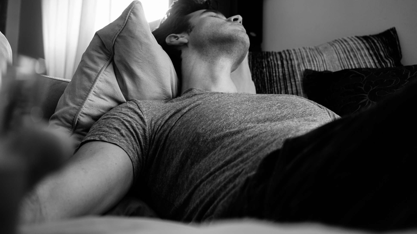 Black and white picture of a man passed out asleep on a couch with his head on a pillow