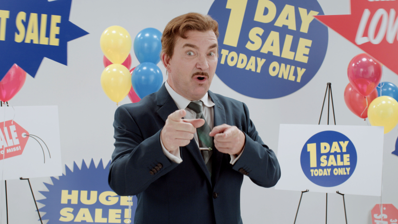 Salesman with a mustache pointing at you standing in front of a bunch of sale signs that say things like huge sale, 1 day sale, & today only