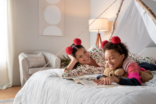 Mother and daughter laying in bed in their pajamas reading a book under a blanket fort