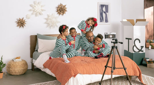 Family in holiday pajamas on top of a bed, getting ready to take holiday pictures.