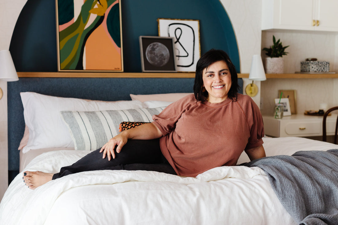 Designer Rebecca Plumb sitting on her Tuft and Needle bed showing off her new bedroom