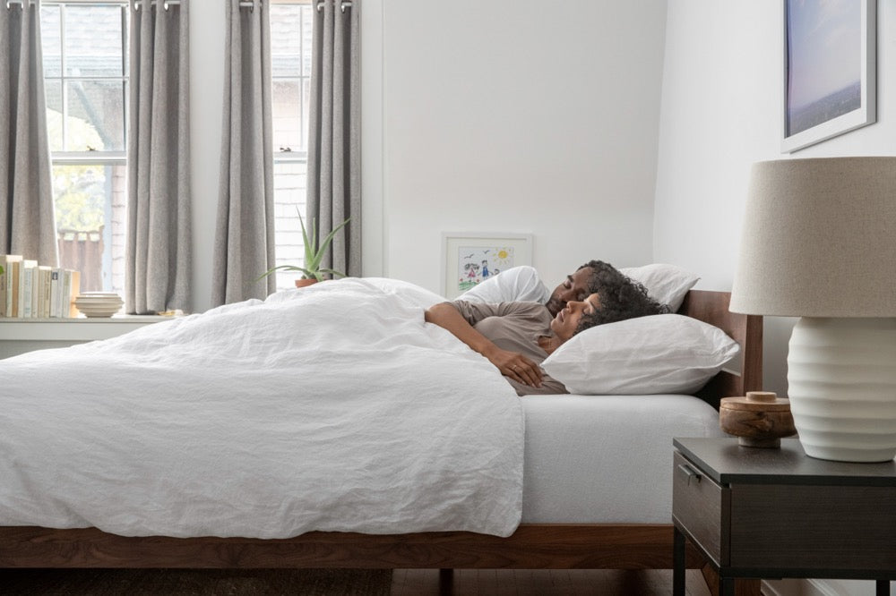 Couple cuddling in a bed made with white bedding