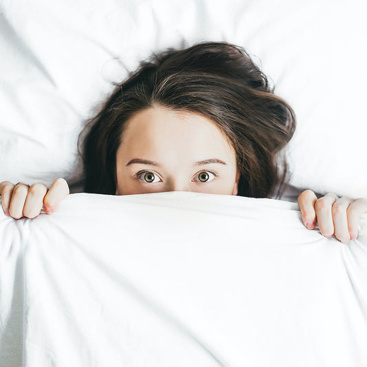 Overhead view of a woman hiding under white covers with only her eyes showing