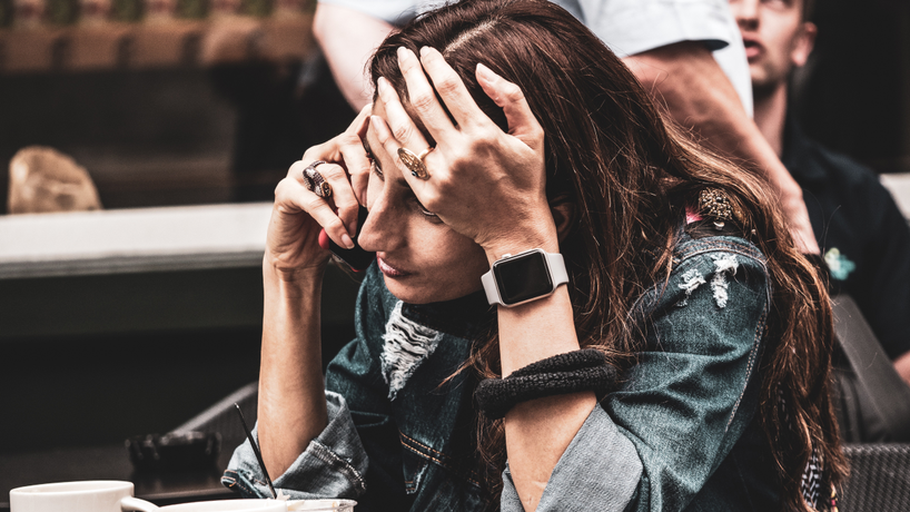 Woman on her phone with one of her hands on her head looking a little stressed out