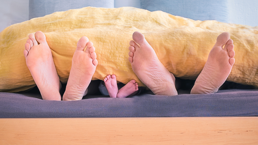 Two pairs of adult feet and one pair of a childs feet sticking out from a yellow comforter
