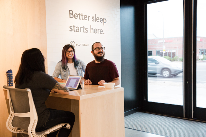 Two customers checking in at the front desk of a Tuft & Needle retail store