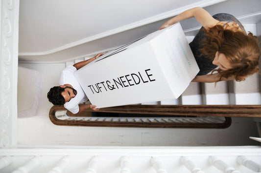 Arial photo of a couple carrying a Tuft & Needle Mattress in a Box up a flight of stairs