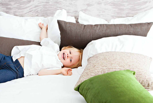 A child smiling laying on a bed with a bunch of pillows