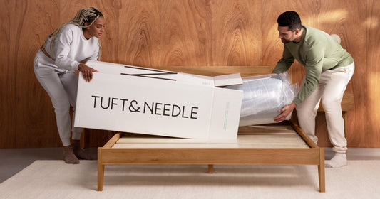 Man and woman taking a Tuft & Needle mattress out of its box and putting it on a bed frame