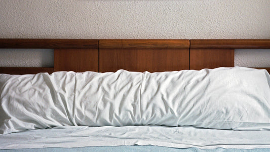 Body pillow in a white body pillowcase leaning up against a dark wood headboard