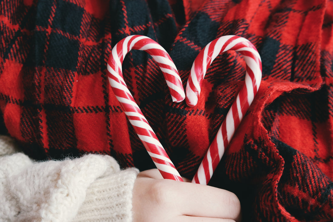A hand holding two candy canes together in the shape of a heart against a red flannel shirt