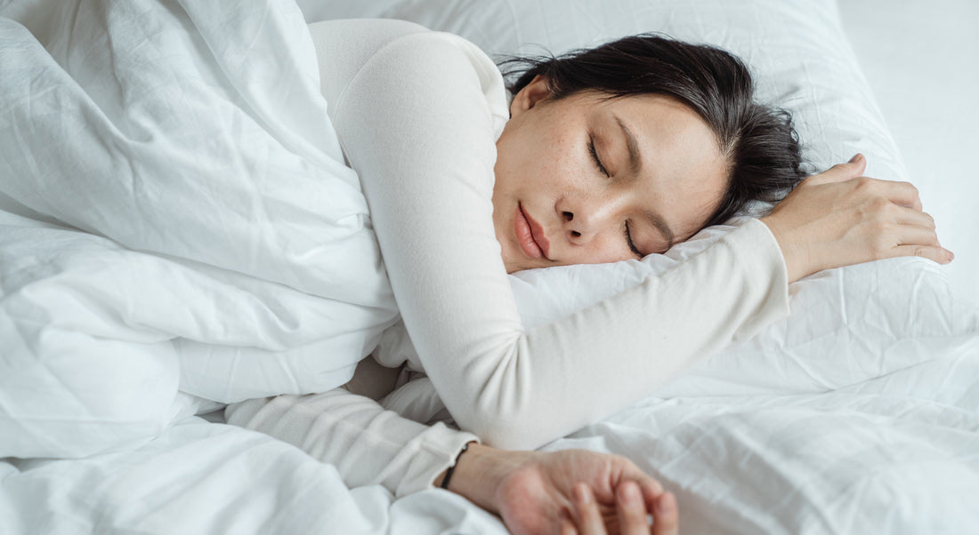 Woman sleeping in a bed with white covers and while pillow wearing a long sleeve white shirt