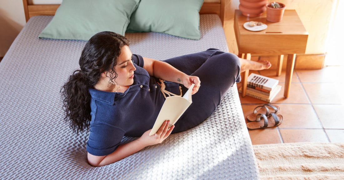 Woman reading a book laying on an unmade Tuft & Needle mattress