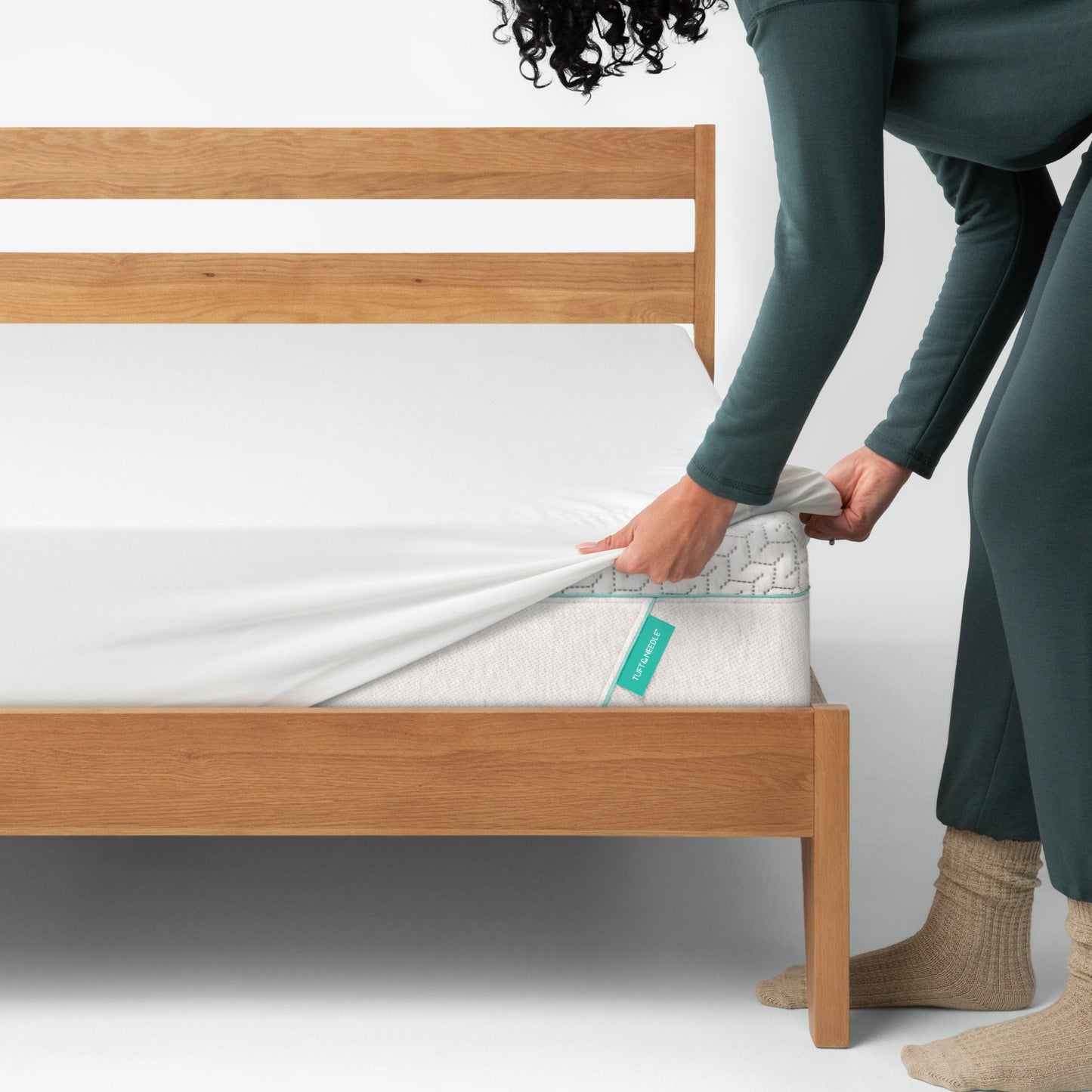 Woman placing a mattress cover on top of a Tuft and needle mattress placed in a brown bed frame