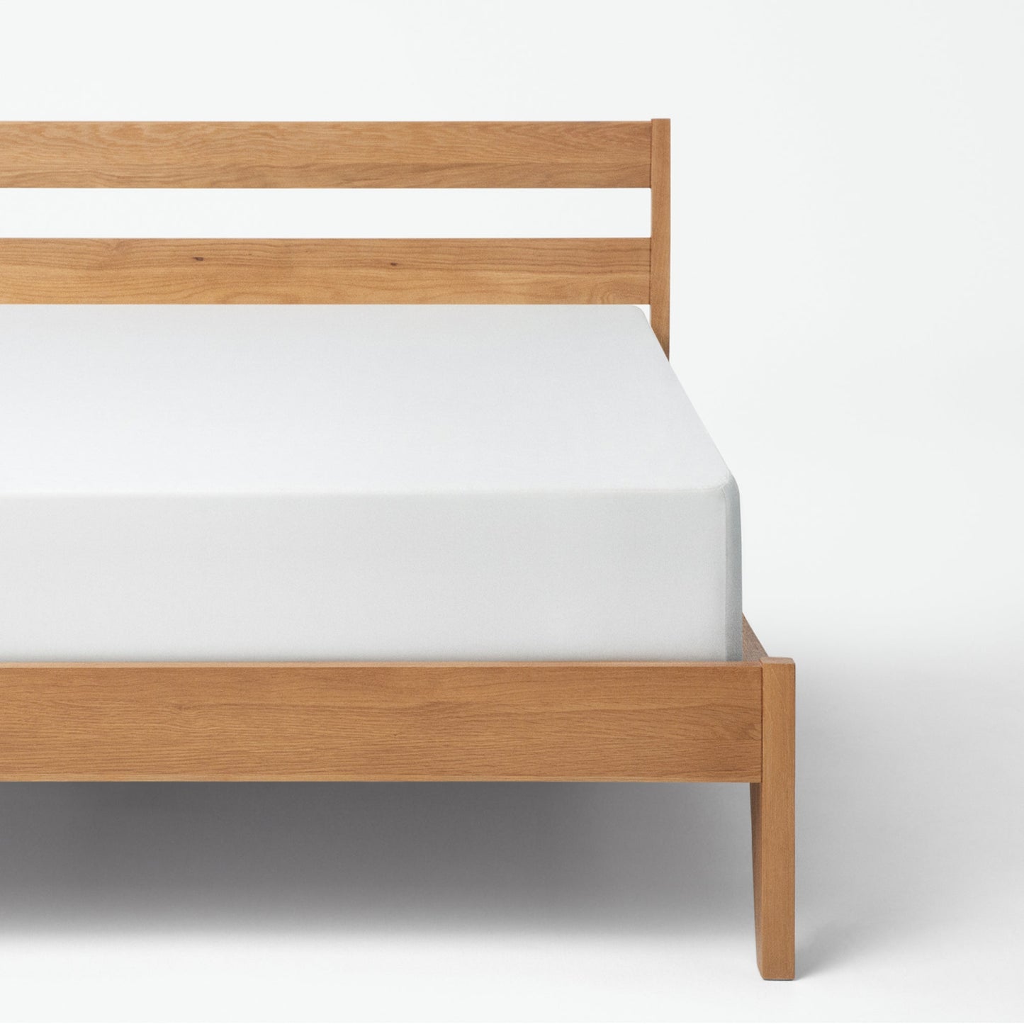 Tuft and needle mattress placed in a brown bed frame with a mattress cover on the mattress