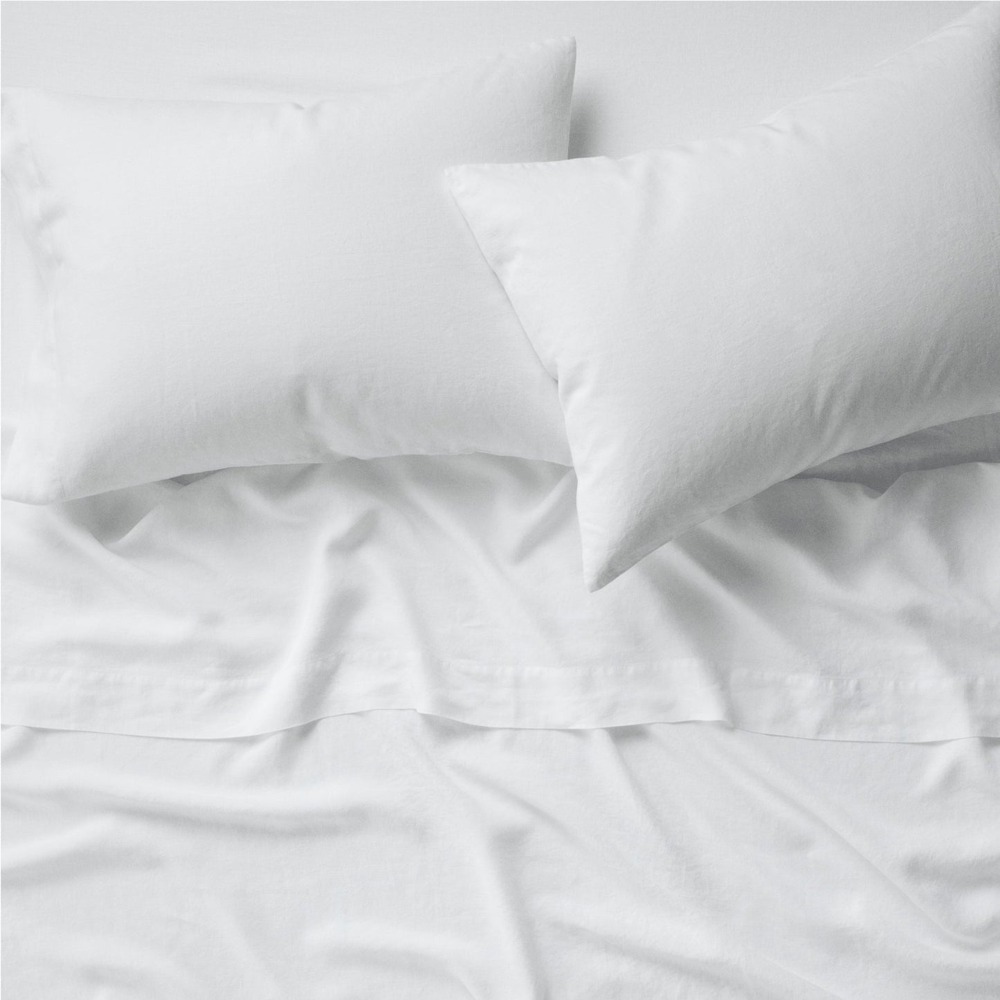 Two pillows on a bed dressed in the Tuft and Needle Hemp Pillowcase Set||color:cloud