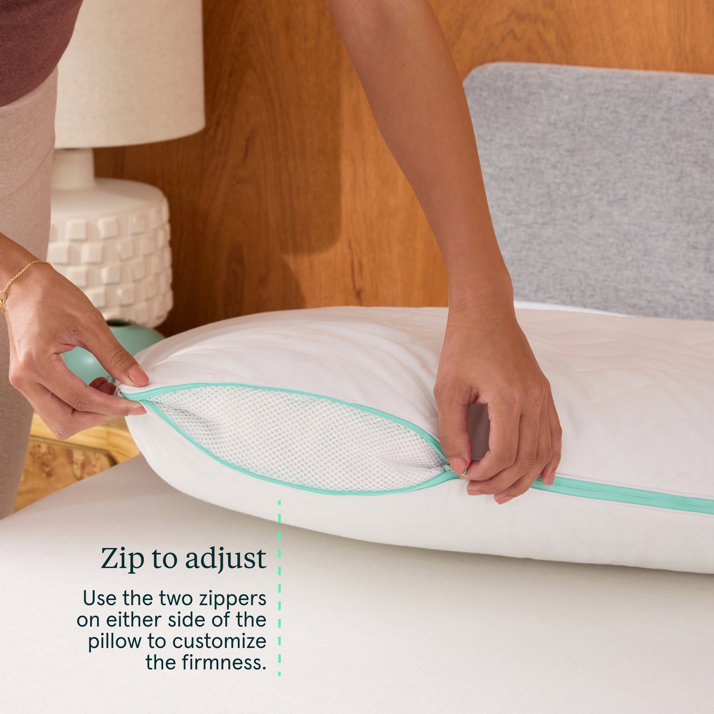 Person adjusting a white Tuft & Needle Zip Comfort pillow with zippers on a bed, with text indicating how to use the zippers.