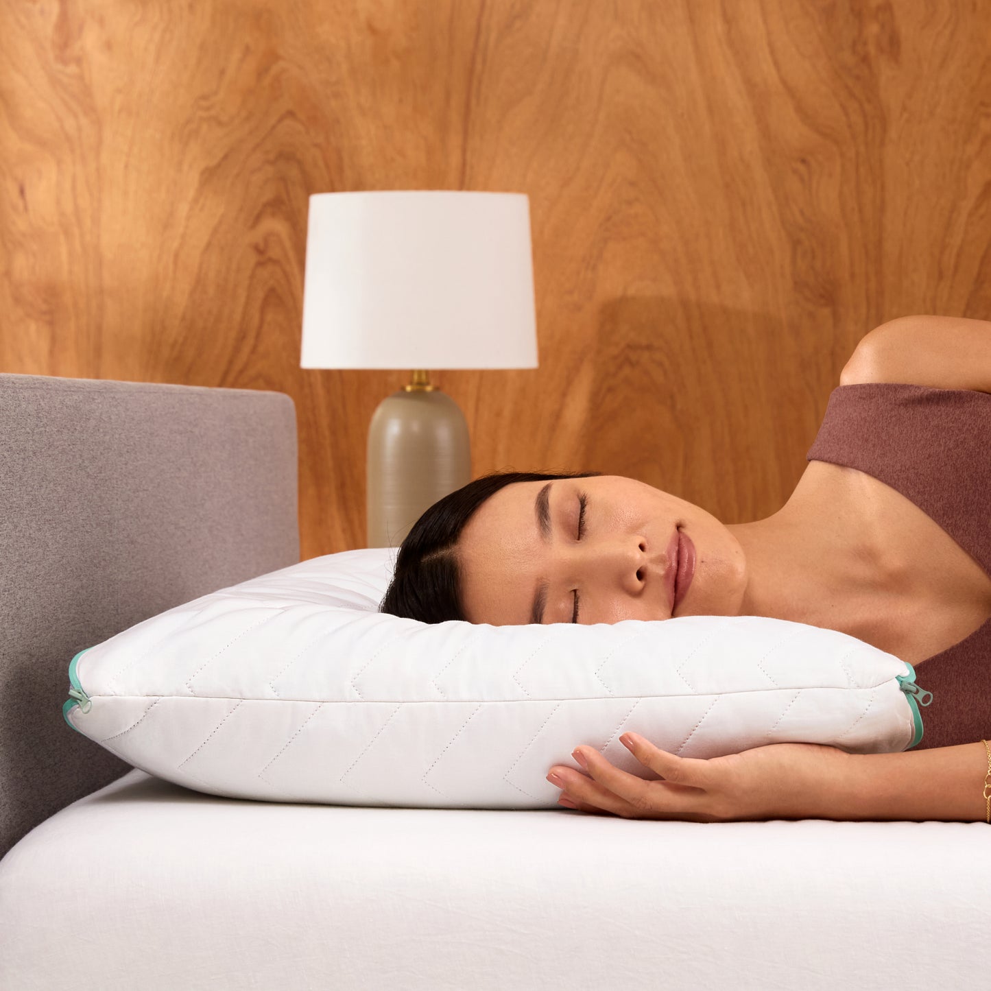 Woman lying on a bed with a white Tuft & Needle zip comfort pillow against a Tuft & Needle bed frame.