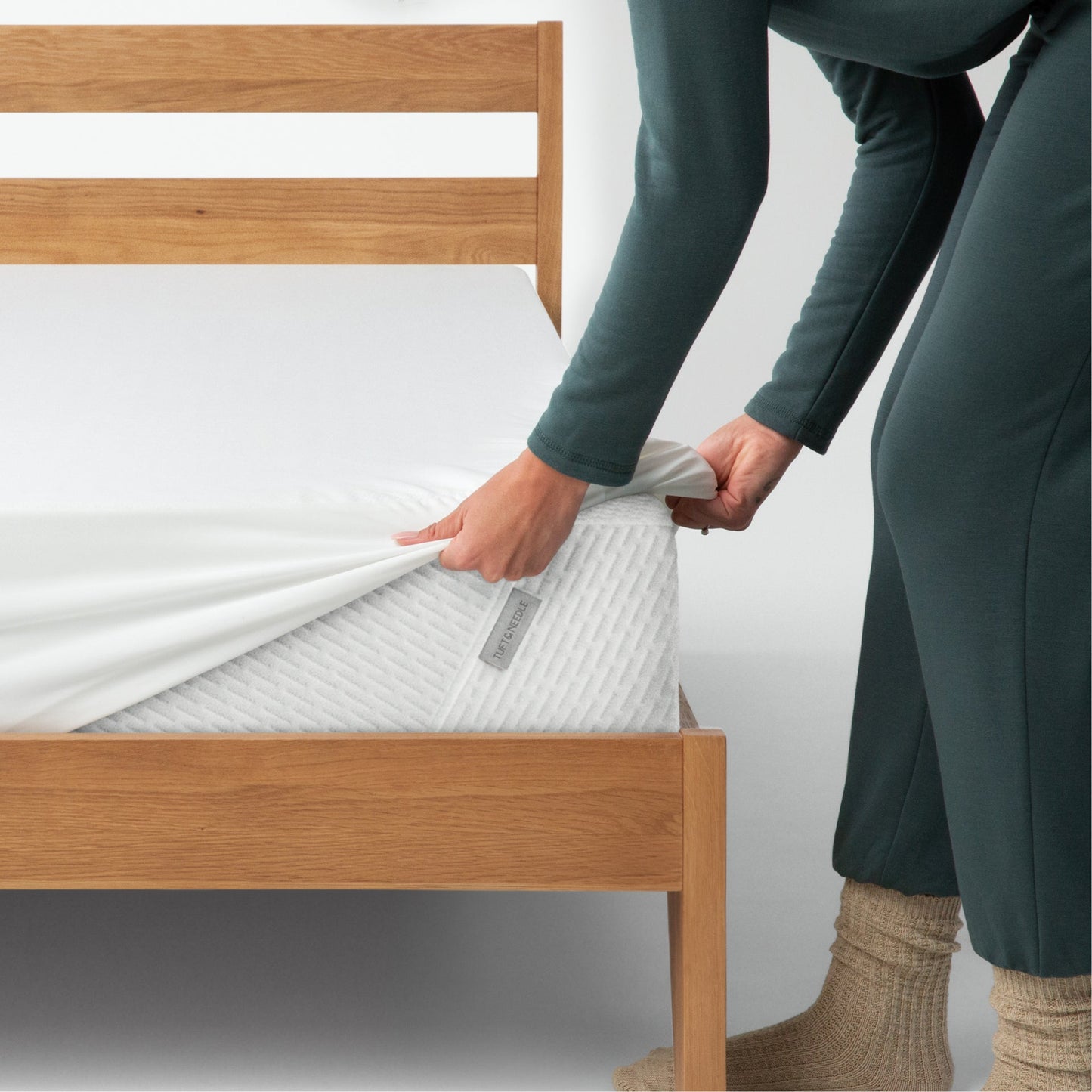 A person putting the Tuft and Needle Mattress Protector on their bed