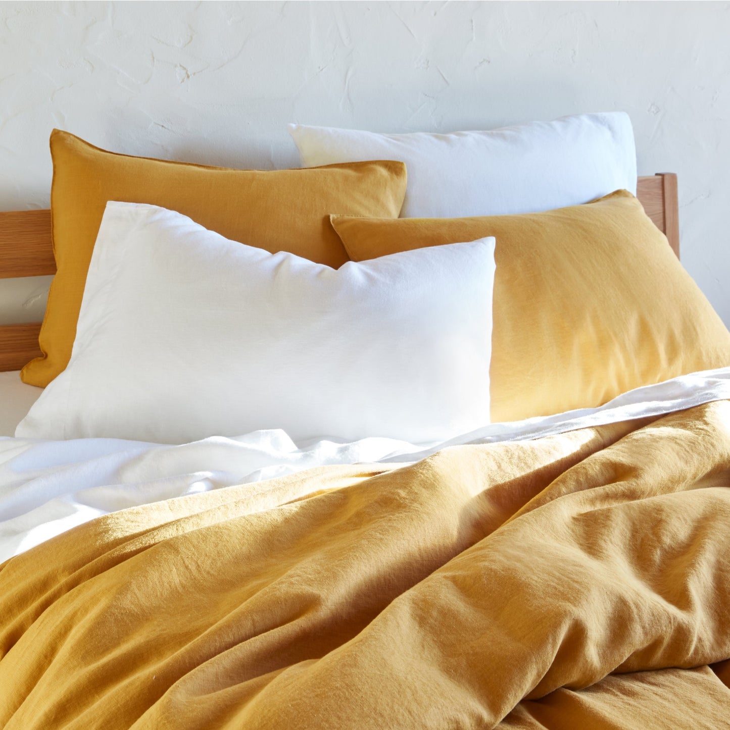 Four pillows on a bed dressed in the Tuft and Needle Hemp Pillowcase Set||color:cloud