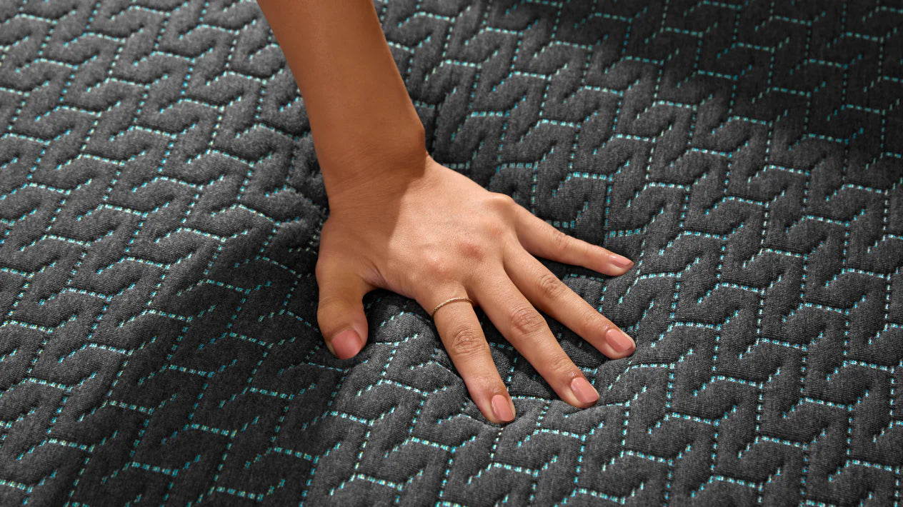 Womans hand pressing down on the top of a hybrid mattress