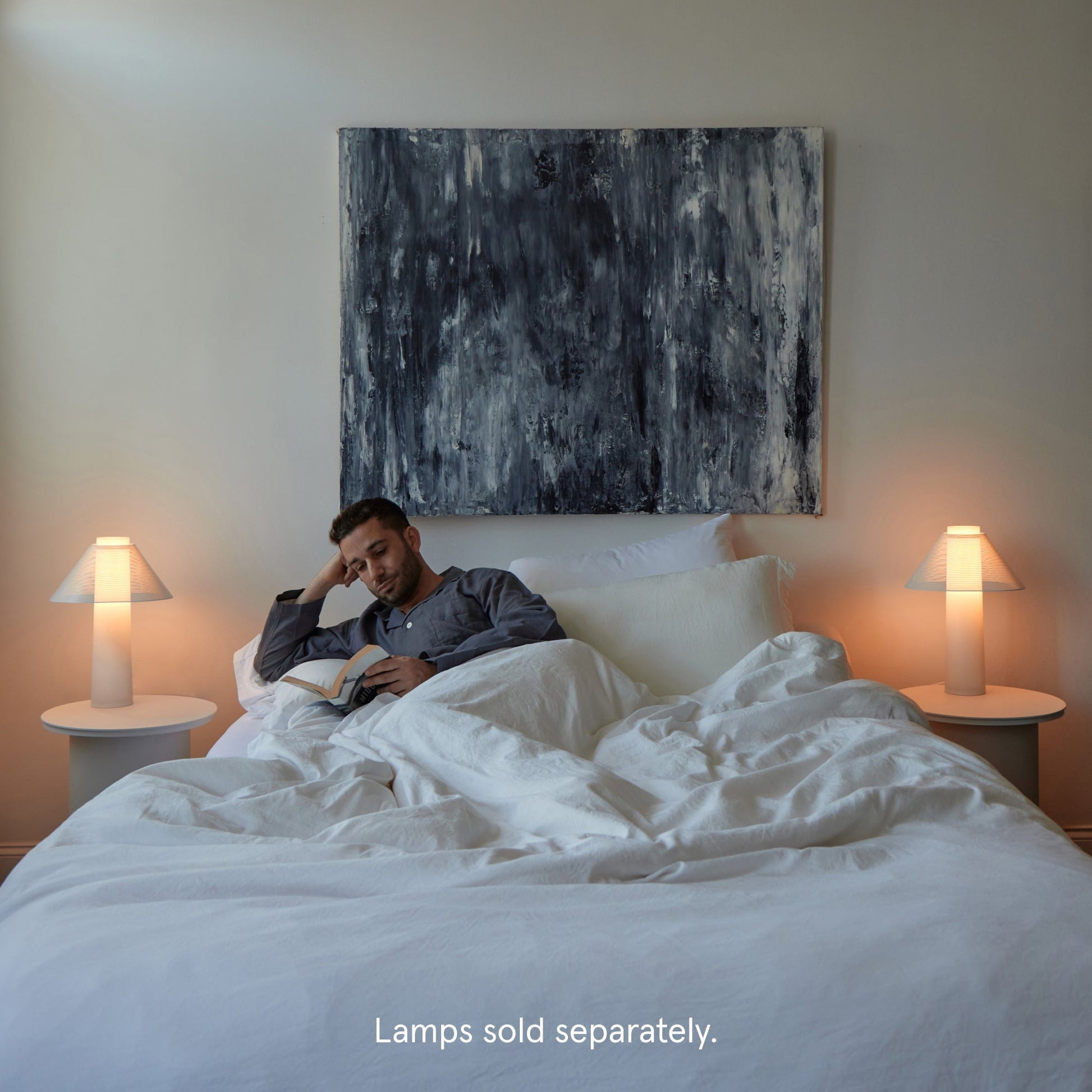 Man laying on a Tuft and Needle mattress with 2 Loftie Lamp on both sides on the bed on end tables.