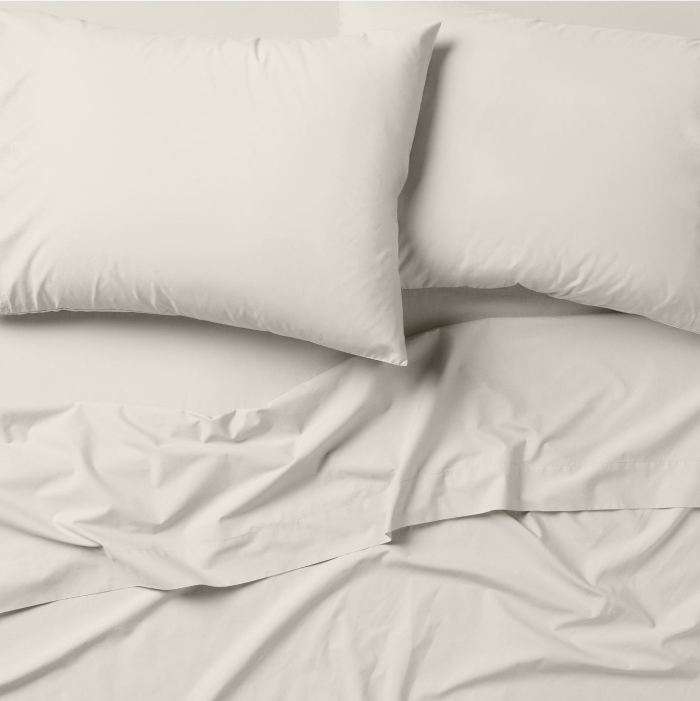 The Tuft and Needle Classic Percale Pillowcase Set, 2 pillows in a pillowcase on top of a spread out sheet || color: Sand