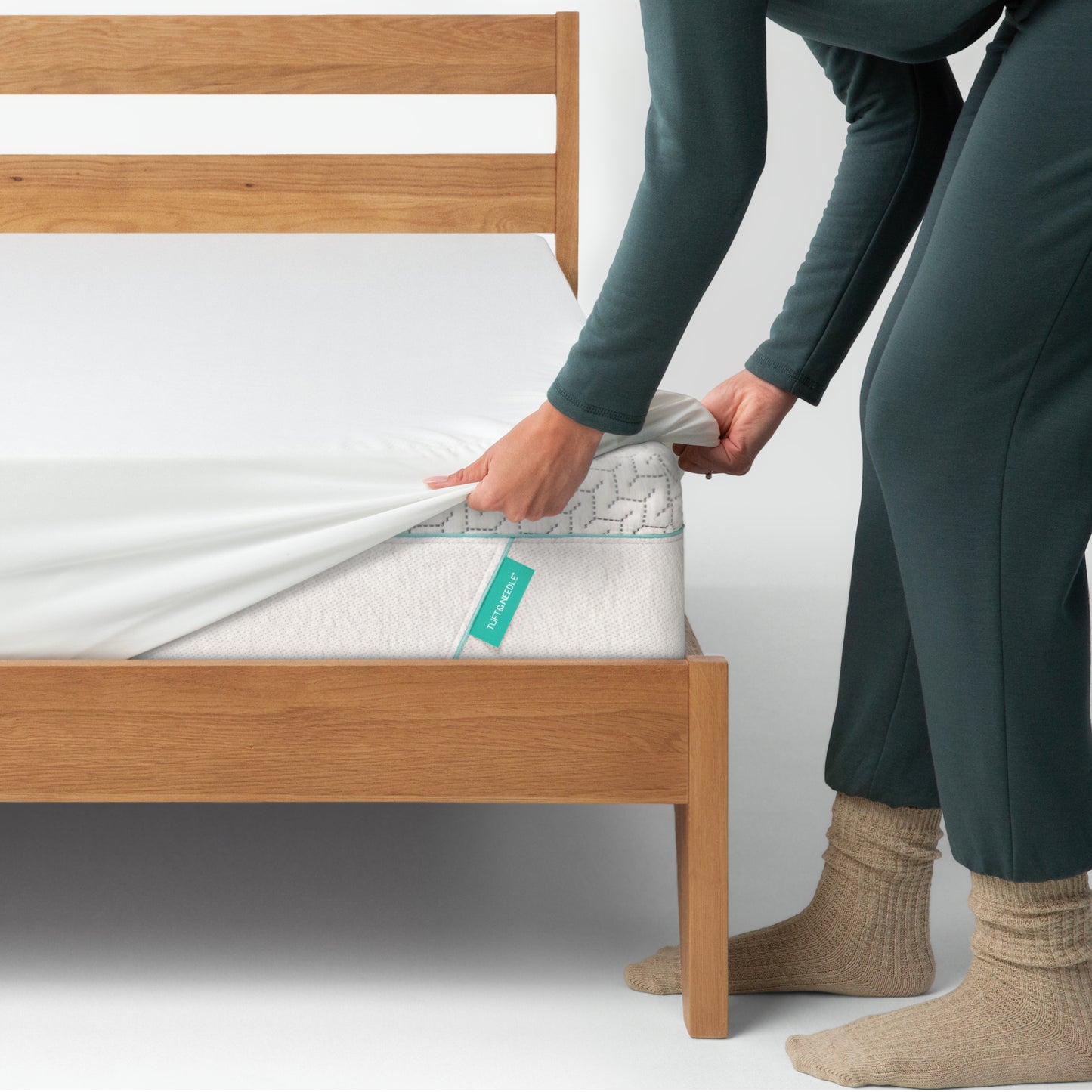 Woman putting a Tuft and Needle mattress on a Tuft and Needle Original  mattress on a wooden bed frame.