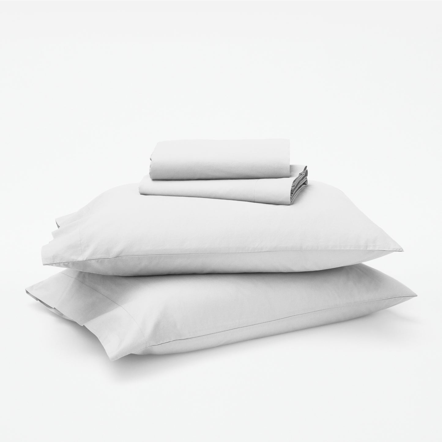 The Tuft and Needle Classic Percale Sheet Set, 1 sheet and pillowcases stacked on top of 2 pillows || color: Cloud