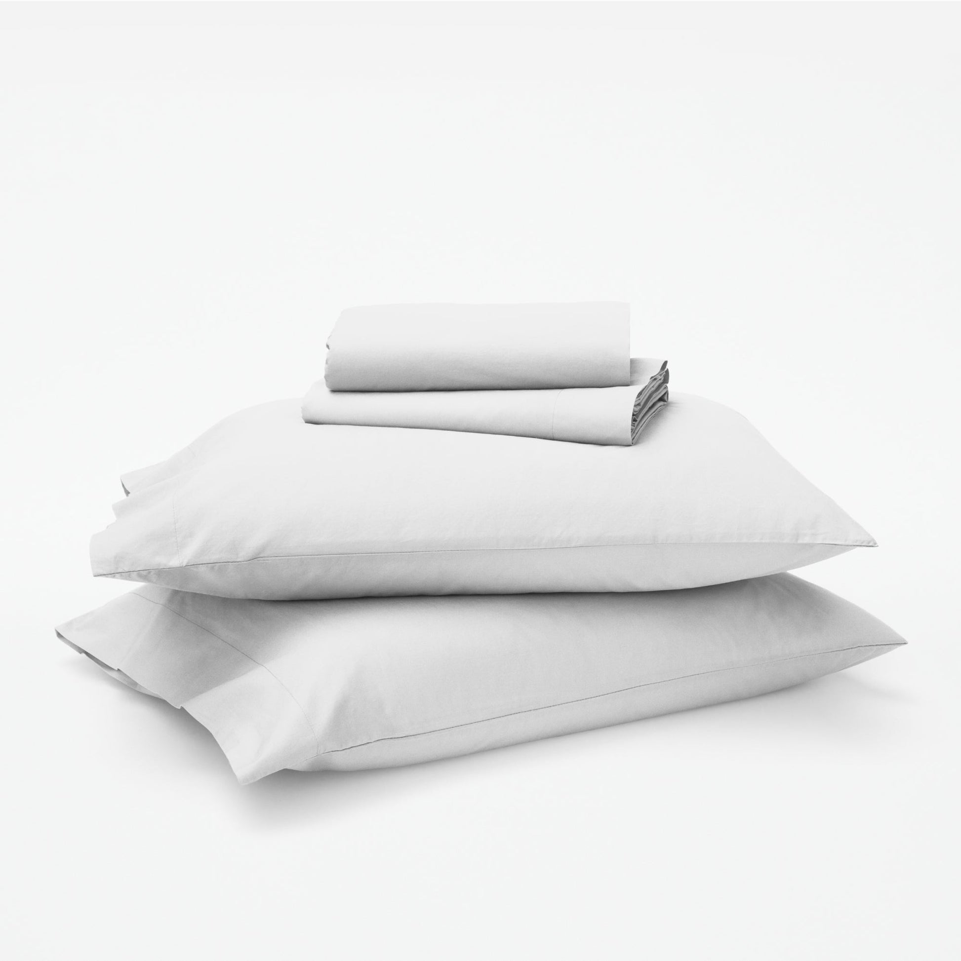 The Tuft and Needle Classic Percale Sheet Set, 1 sheet and pillowcases stacked on top of 2 pillows || color: Cloud
