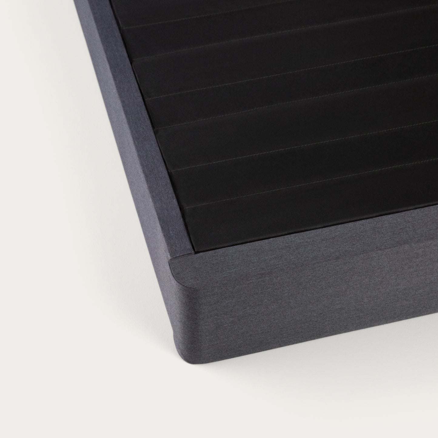 Corner of a Tuft & Needle black colored mattress foundation on a white background