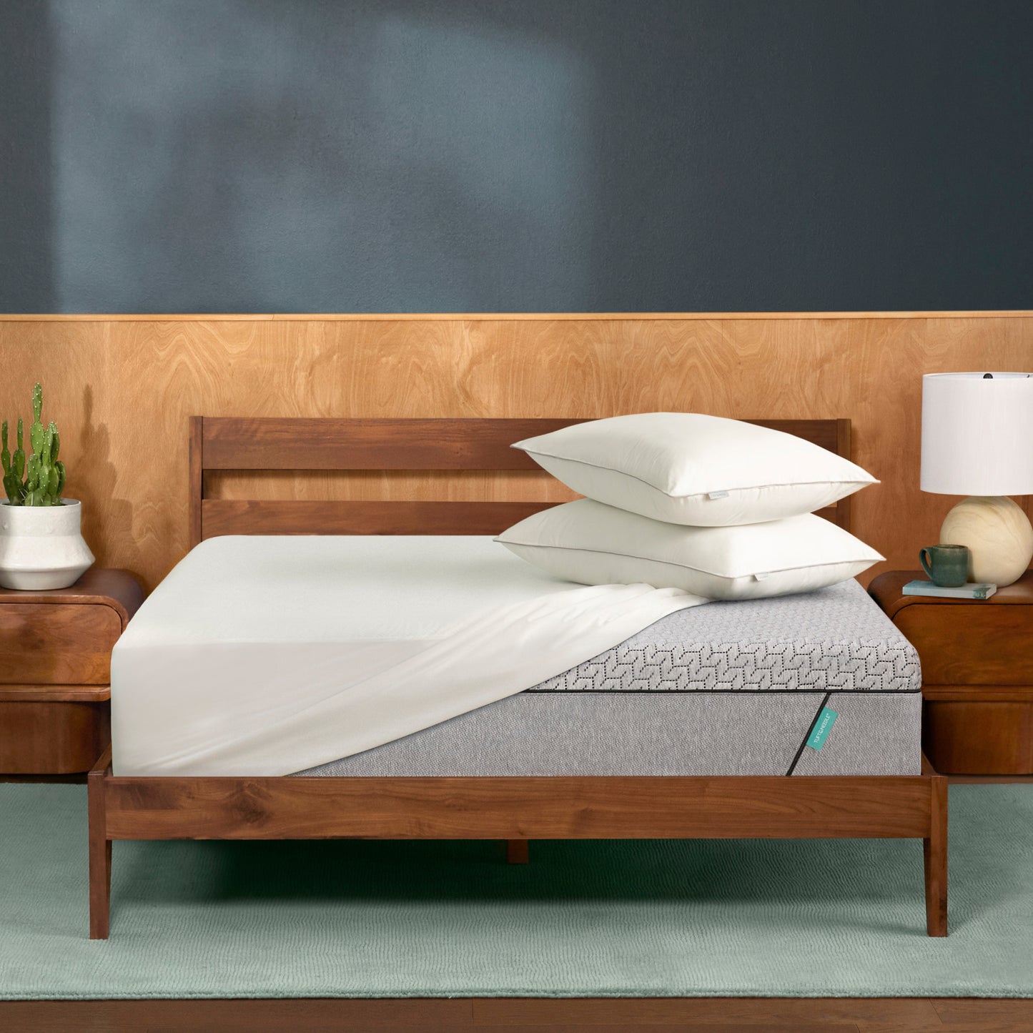 Wooden Tuft & Needle bed with gray mattress and white pillows in a bedroom setting.