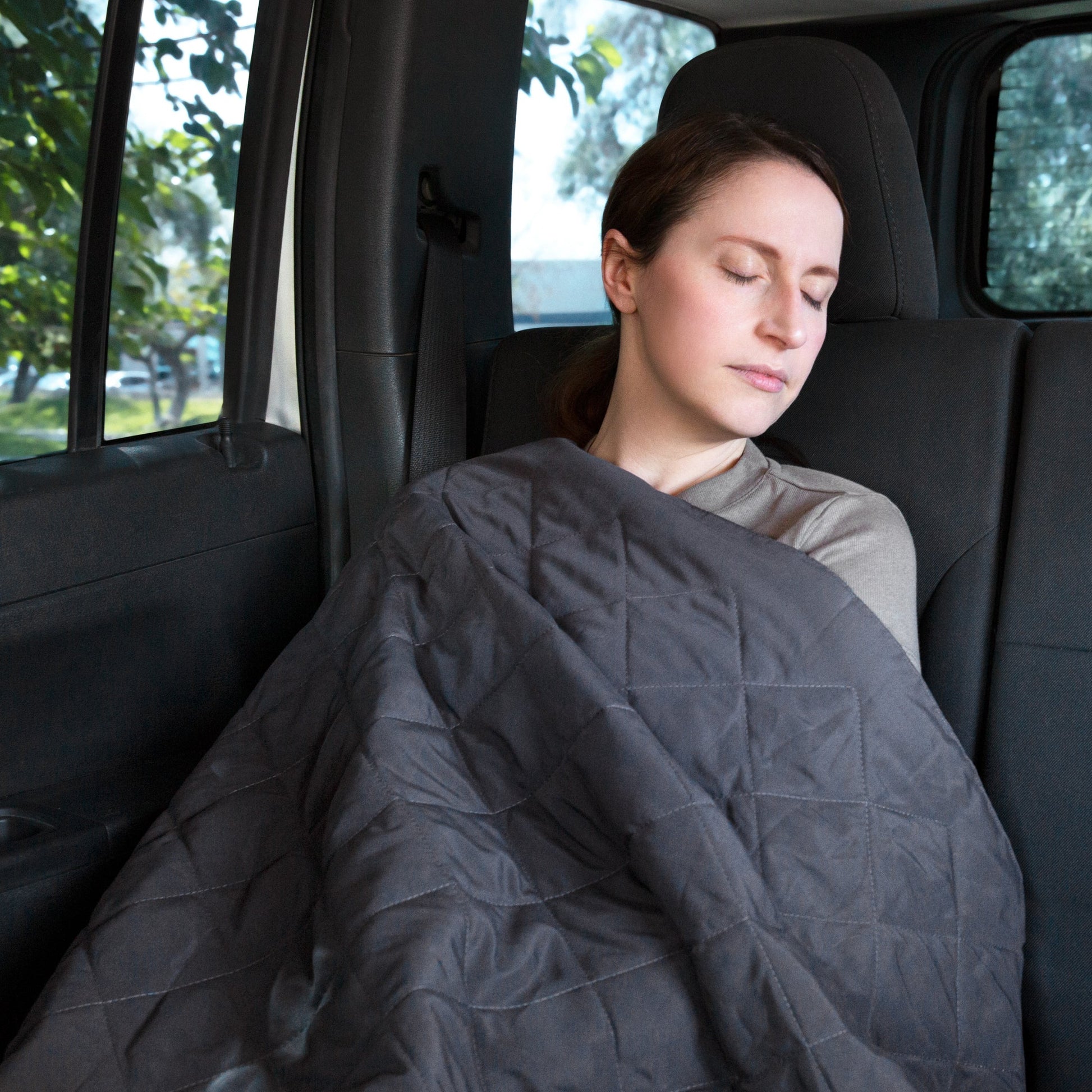 Woman sleeping in a car wrapped up in the Anywhere Travel Blanket