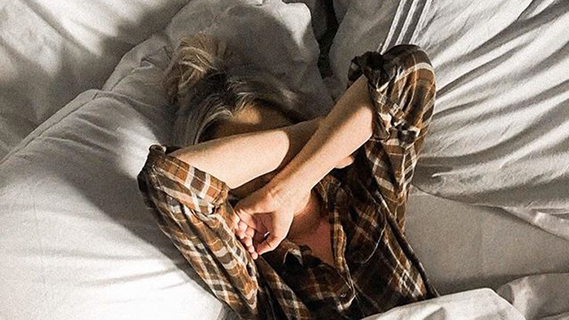 Woman laying in bed with her arms over her head not wanting to get up