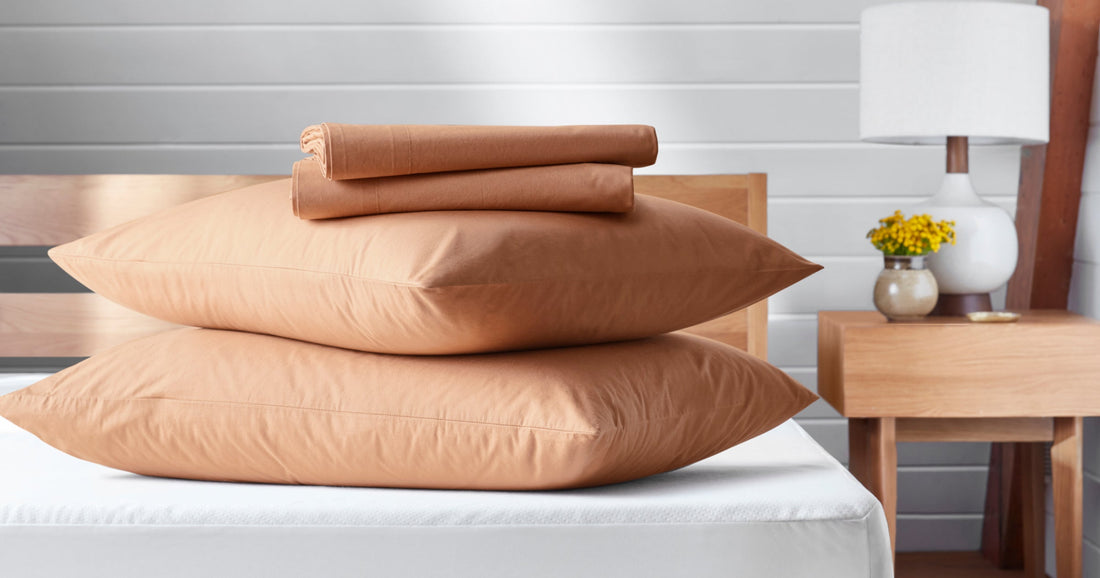 On top of a T&N mattress & bed frame sits two T&N pillows in pillow cases stacked on top of one another with folded sheets on top of the pillows. The sheet set color is Canyon.
