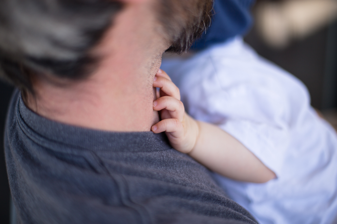 Man holding a baby who has its hand on his neck