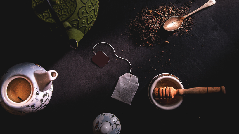 Teapots, a spoon, honey and tea bag on a dark table.