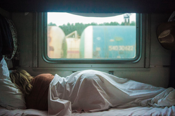 Someone sleeping on their side with their back facing the camera next to a window