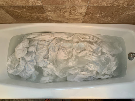 Arial photo of soaking aka laundry stripping Tuft & Needle Linen sheets in a bathtub full of water.