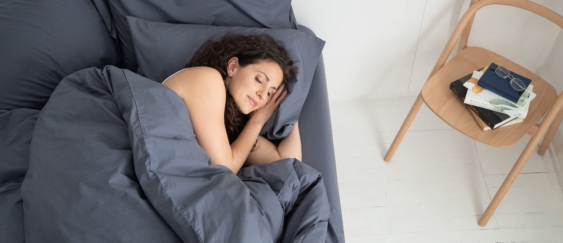 Woman sleeping on her side in a bed made with grey bedding