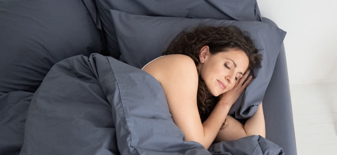 Woman sleeping on her side on blue/grey Tuft & Needle Bedding