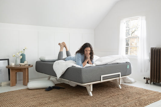 Woman laying on her stomach with legs bent up on top of a Tuft & Needle mattress and adjustable bed frame in a bedroom