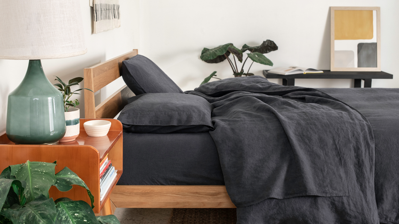 Side view of a bed in a bedroom with a night stand, lamp and mirror made with grey linen bedding from Tuft & Needle