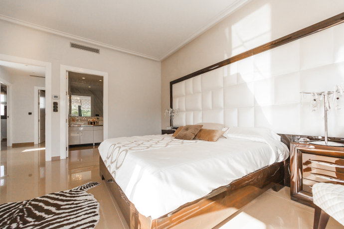 Picture of a bedroom with a zebra rug on the floor, bed made in white bedding and a white puffy headboard outlined in wood that takes up most of the wall