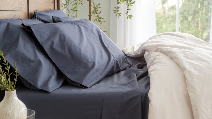 The side of a made bed with blue pillowcases and sheets and a white comforter folded down inviting you in