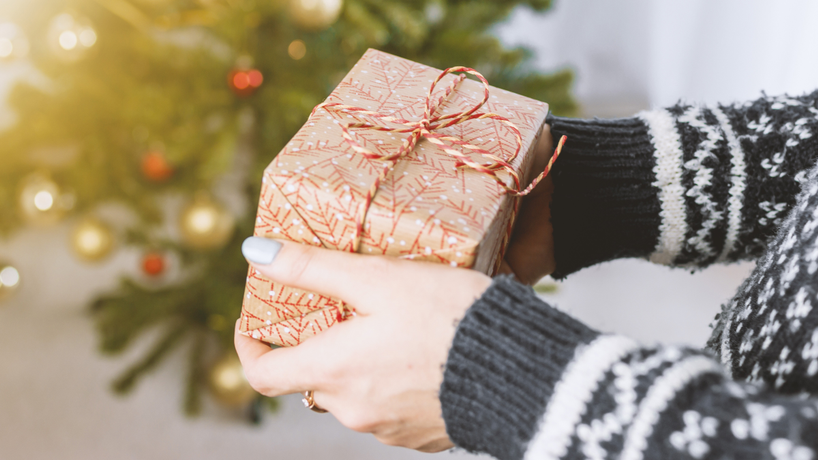 Hands holding a wrapped present with a decorated tree in the background